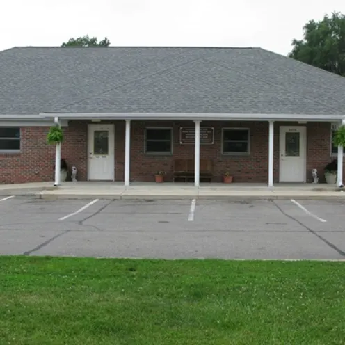 The front of the facility, a brick building, parking lot, and a lawn.